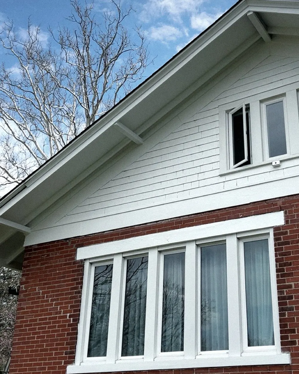 After: smooth white gable siding and trim over red brick, a row of white-framed windows.