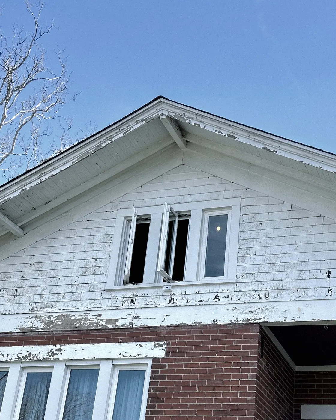 Before: white clapboard gable with paint peeling off the siding and trim, three small windows.