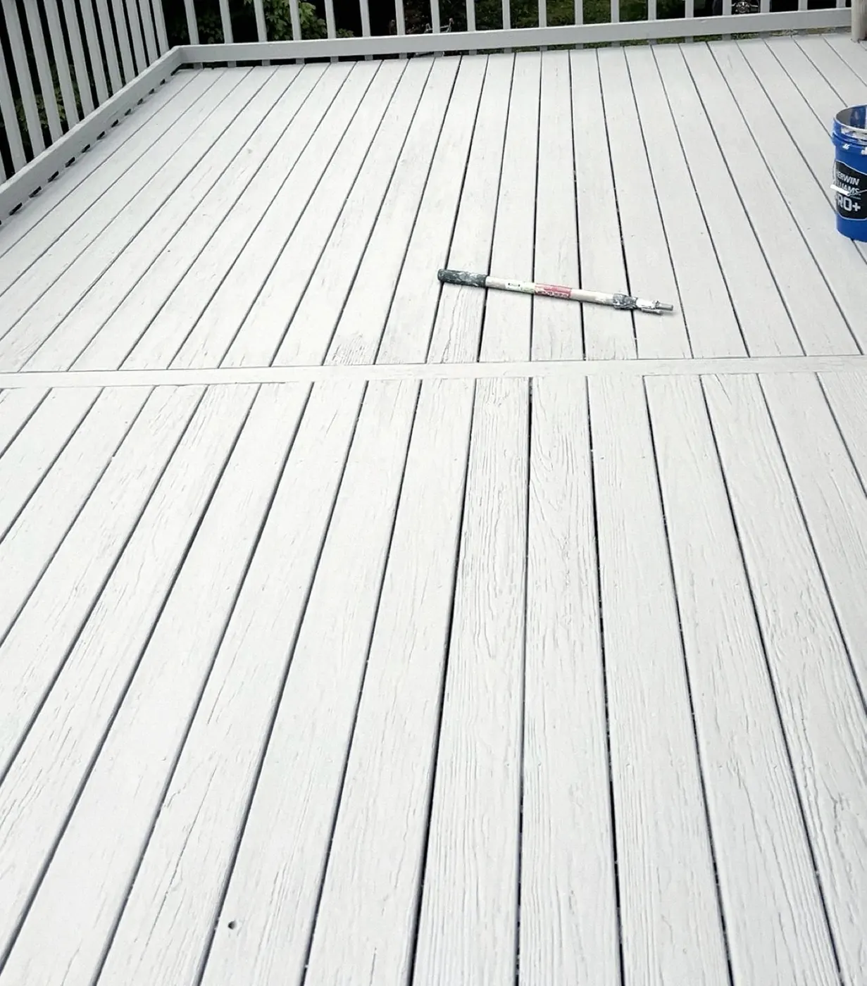After: deck boards in an even light gray finish, a paint bucket and a pole at the edge of the frame.