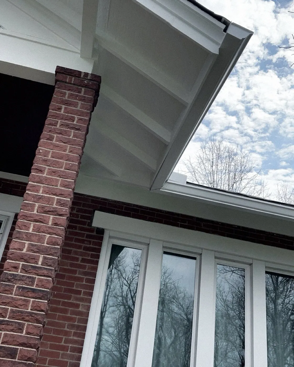 Brick porch column under a freshly painted white soffit, white window frames below.