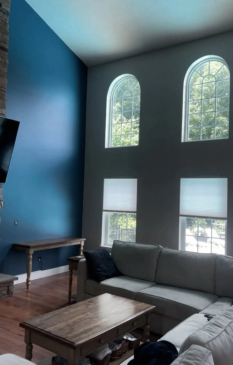 Two-story great room with a deep blue wall, tall arched windows, a sectional sofa and coffee table on hardwood.