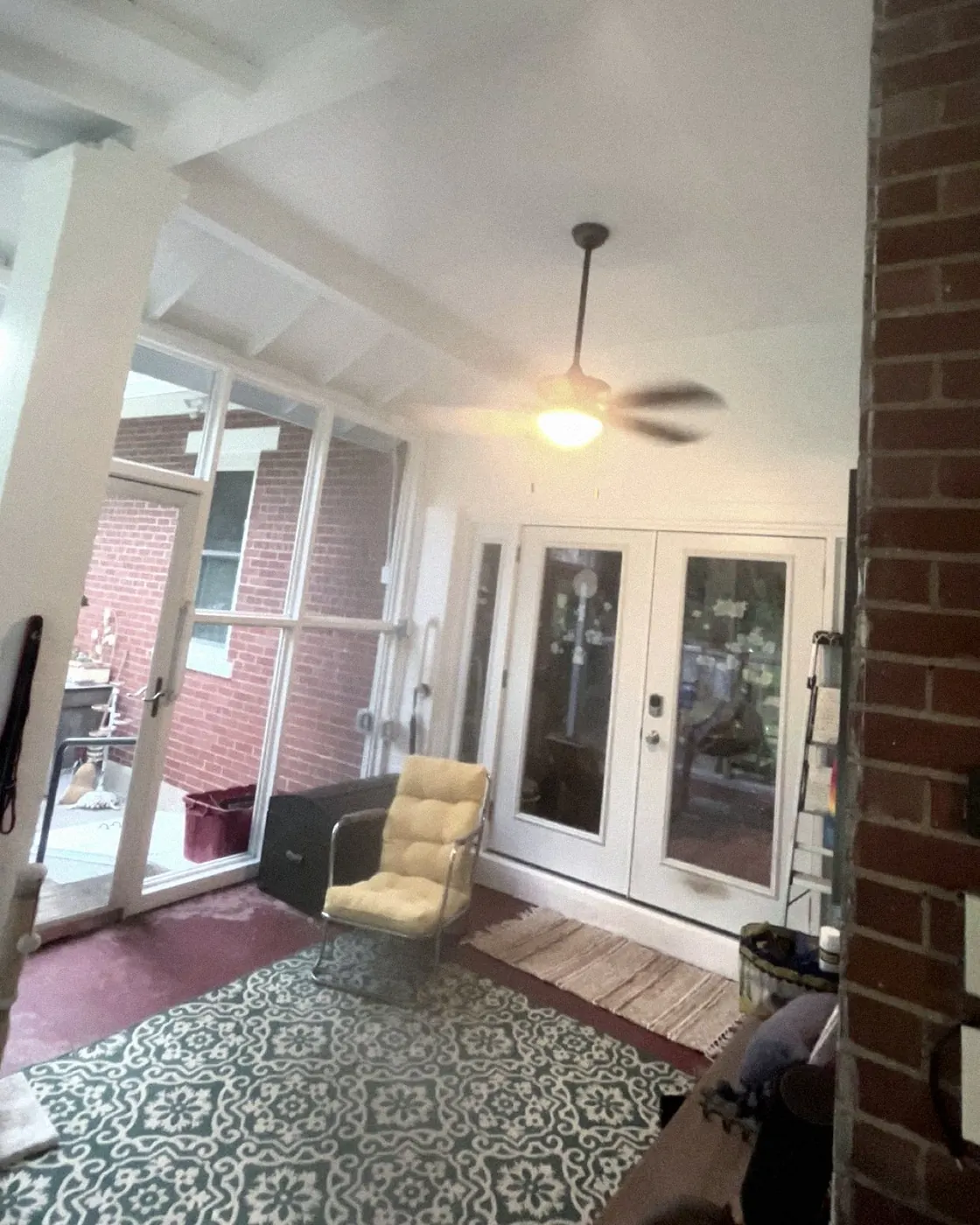 Sunroom with a white beamed ceiling, ceiling fan, and French doors, patterned rug on the floor.
